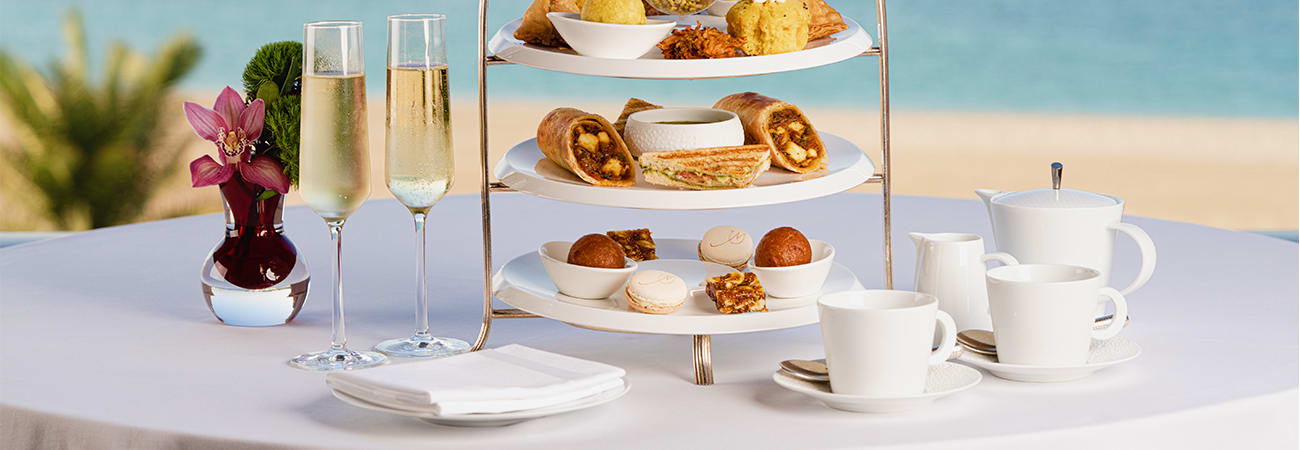 Elegant afternoon tea service at Emirates Palace with tiered white stand displaying pastries, scones, and sandwiches, champag